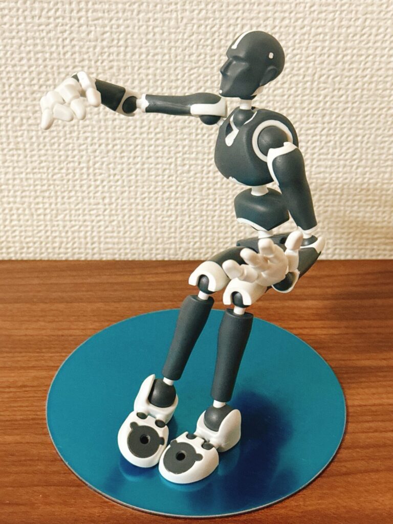 Stickybonesのフィギュアが青い台座の上で片腕を伸ばしたポーズを取っている。木のテーブルと淡い壁を背景にした組み立て後の状態。